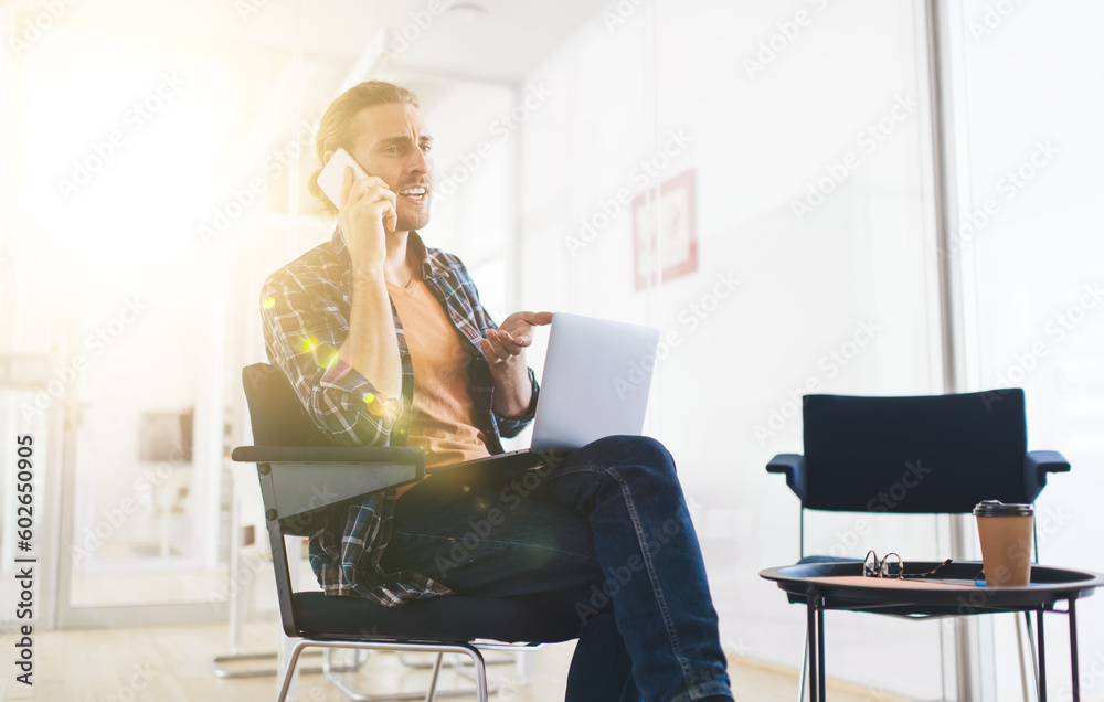 Puzzled male programmer calling to colleague for discussing problems with web startup project working remotely on modern laptop device, serious man using mobile application for talking and phoning