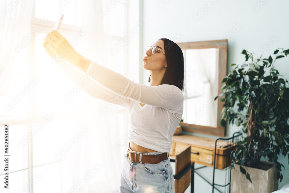 Happy woman taking selfie on smartphone near window