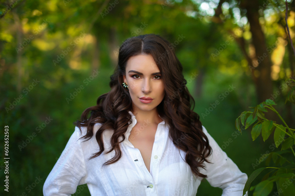 beautiful fashionable brunette woman adult posing in the park on the nature backgraund in white linen shirt beautiful fashionable brunette woman adult posing in the park on the nature backgraund in white linen shirt