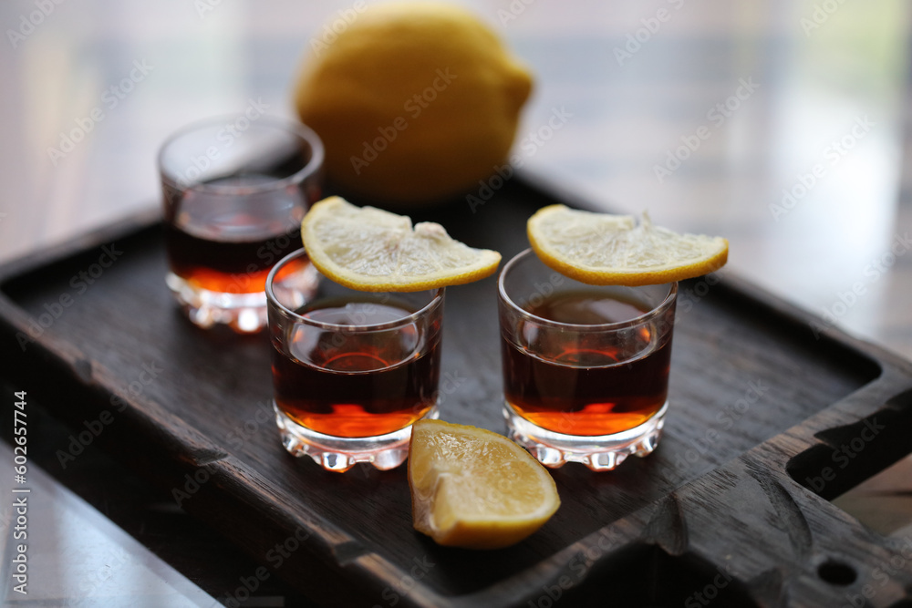 three shot glasses with lemon slices on a wooden plate