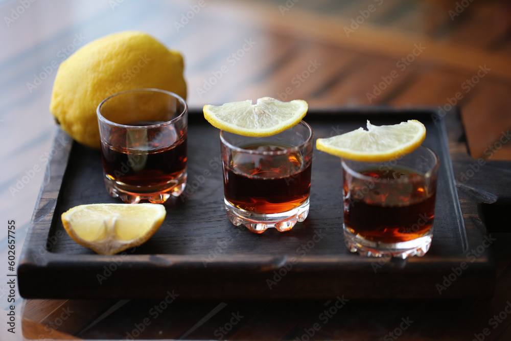 three shot glasses with lemon slices on a wooden plate