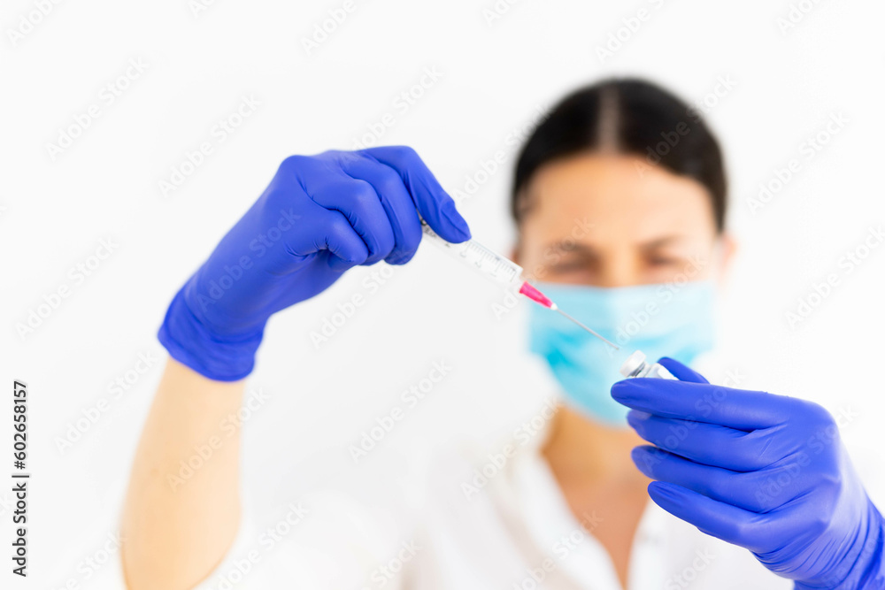 a blue masked brunette doctor or nurse in a hospital working in a clean and sterile asepctic environment in a laboratory with an injection a blue masked brunette doctor or nurse in a hospital working in a clean and sterile asepctic environment in a laboratory with an injection