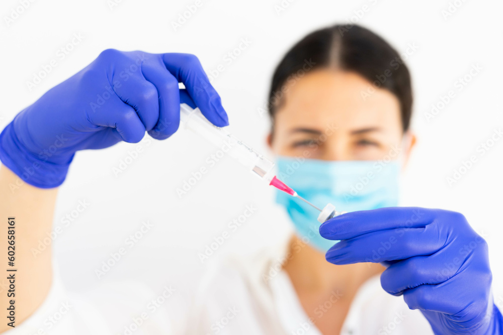 A doctor preparing a vaccine syringe in blue gloves and a mask for a covid 19 vaccination A doctor preparing a vaccine syringe in blue gloves and a mask for a covid 19 vaccination