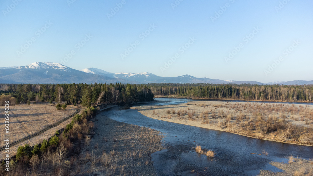 Aerial view of mountain river in taiga. Forest in early spring in sunset time. Siberian or Canadian landscape from above.