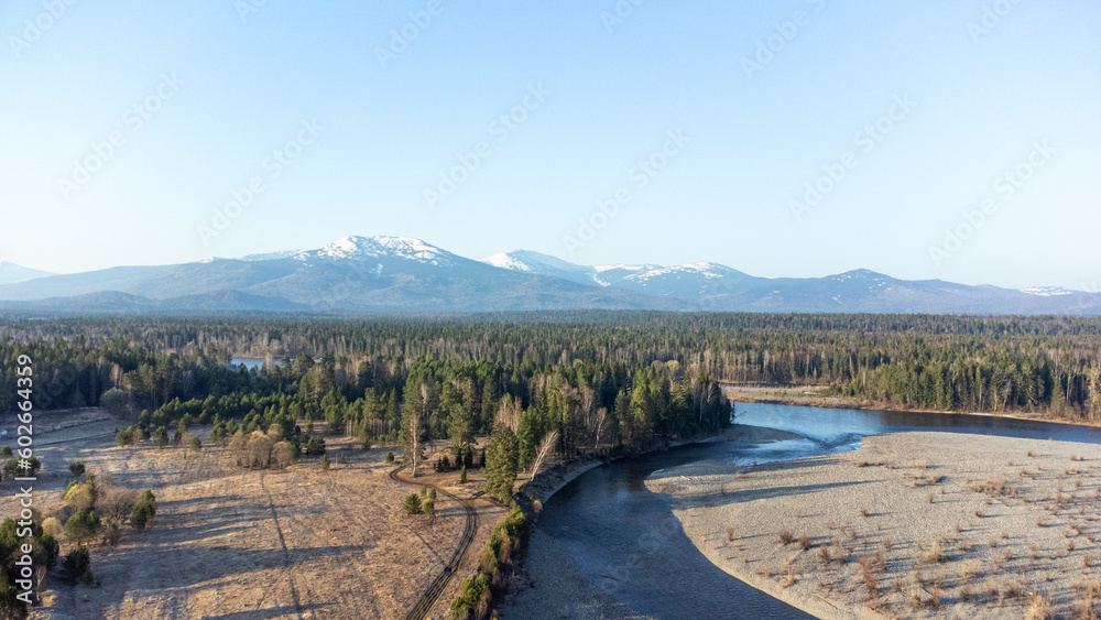 Aerial view of mountain river in taiga. Forest in early spring in sunset time. Siberian or Canadian landscape from above.