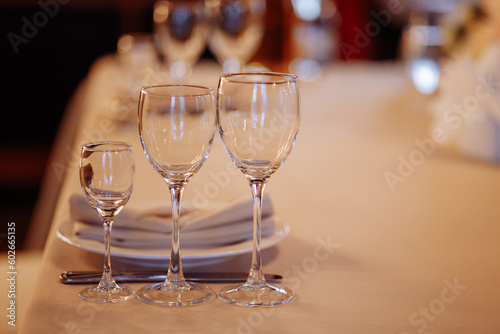 Three crystal or glass goblets on tables served with white ceramic plates and napkins for a banquet at a wedding or other festive event.