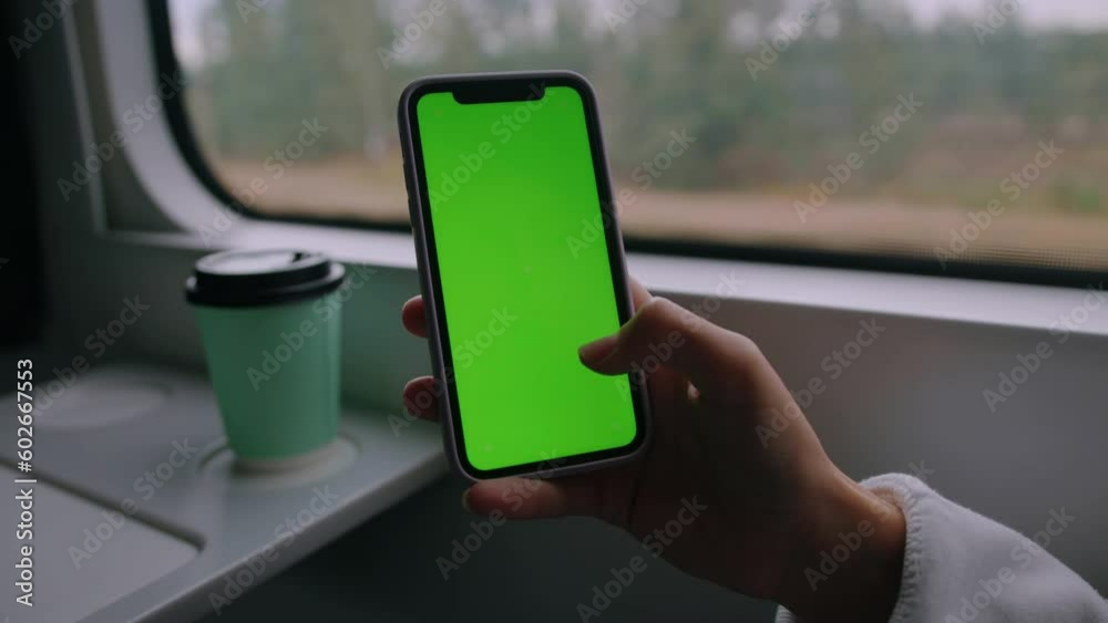 Close-up of the hand of a woman who swaps on the green screen of the phone. The carriage of a modern train