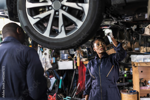 Black car mechanic woman working underneath vehicle in auto repair shop doing Car Maintenance