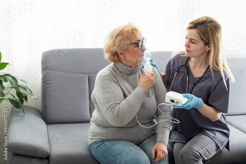 Young girl doctor makes inhalation to an older woman on a white background. Fight nasal congestion and rhinitis. photo