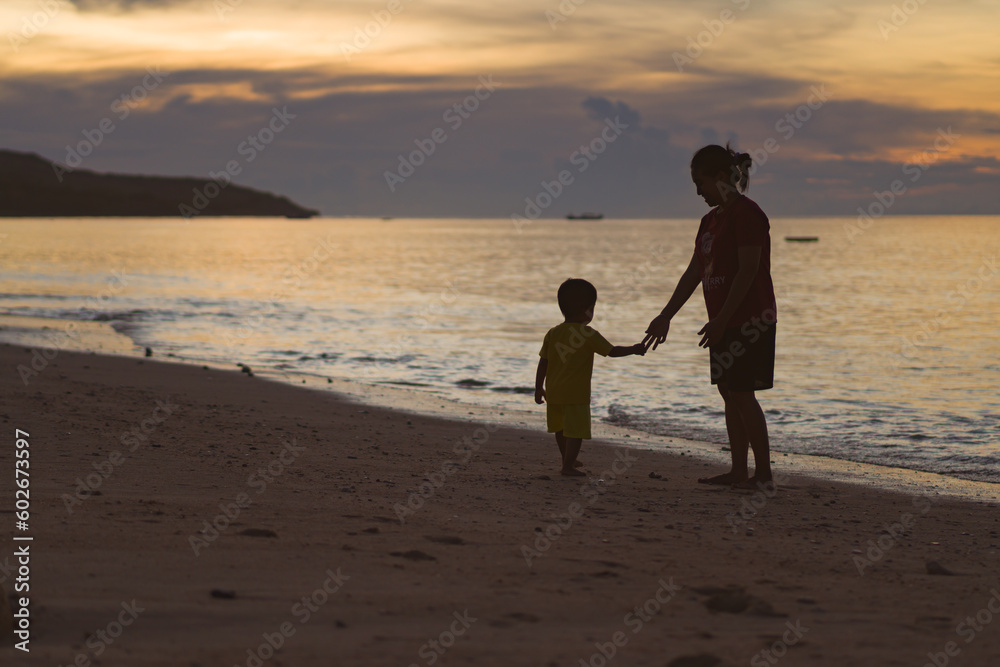 parent and child walk on the beach at sunset