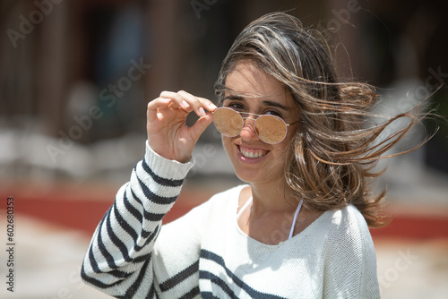 Fotomurale Mujer joven feliz de tez blanca agarrando sus anteojos, de día