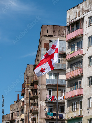 Soviet-era residential building in rural Georgia on a sunny spring afternoon with the Georgian flag flying in the foreground
