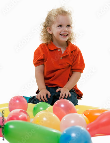 Adorable little three year old boy sitting on the floor with many balloons smiling