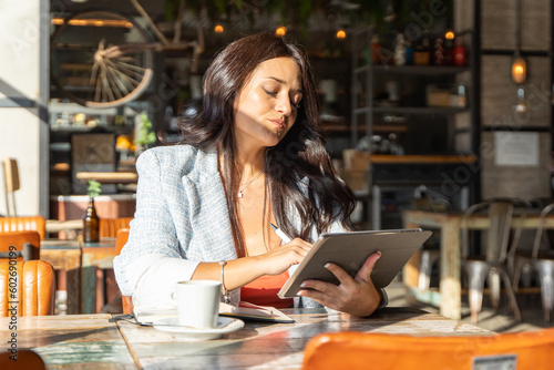 Shocked woman looking with surprise at the digital tablet while sitting in a coffee shop.