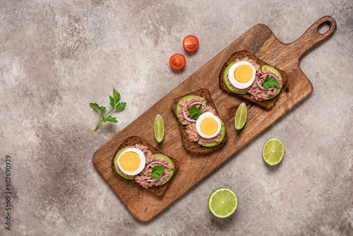 Tuna toast. Open sandwich with tuna, rye bread, avocado and boiled egg on a wooden long board, brown grunge background. Top view, flat lay.