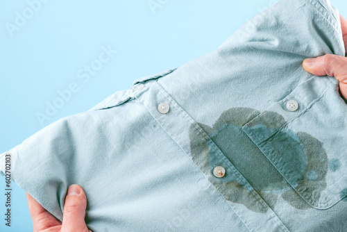 Men hands showing a dirty stain shirt and visual evaluation of stain on clothes on a blue background. Spoiled linen. isolated photo