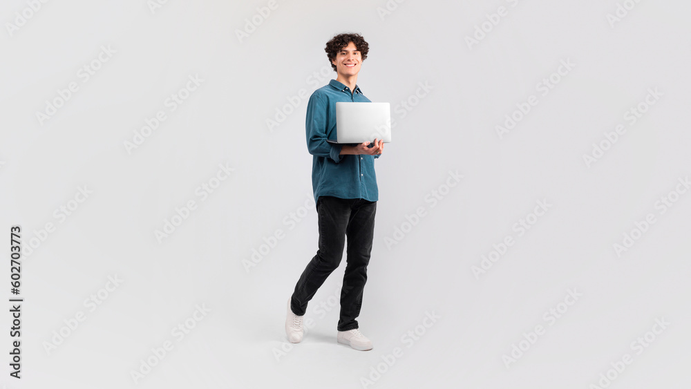 Cheerful Young Man Holding Computer Standing Over Yellow Studio Background Cheerful Young Man Holding Computer Standing Over Yellow Studio Background