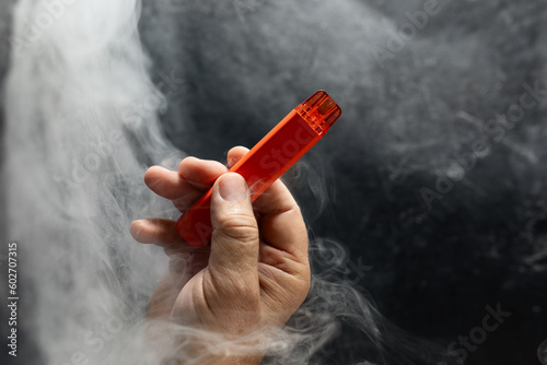 disposable electronic cigarette in a man's hand on a dark background with smoke around. The concept of modern alternative smoking, vaping and nicotine