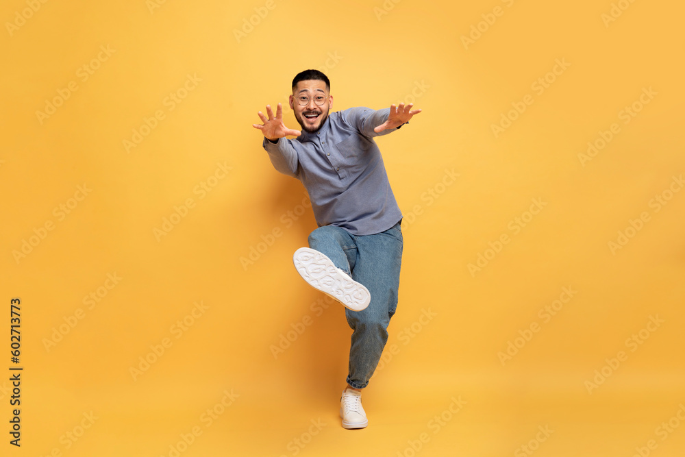 Cheerful young asian man having fun on yellow studio background