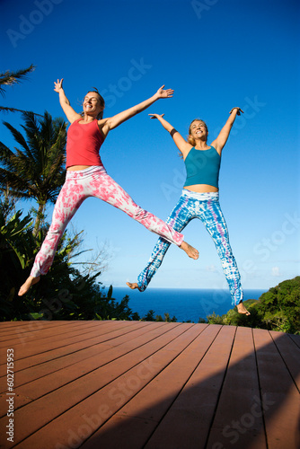 Caucasian mid-adult women jumping into air with arms and legs outstretched.