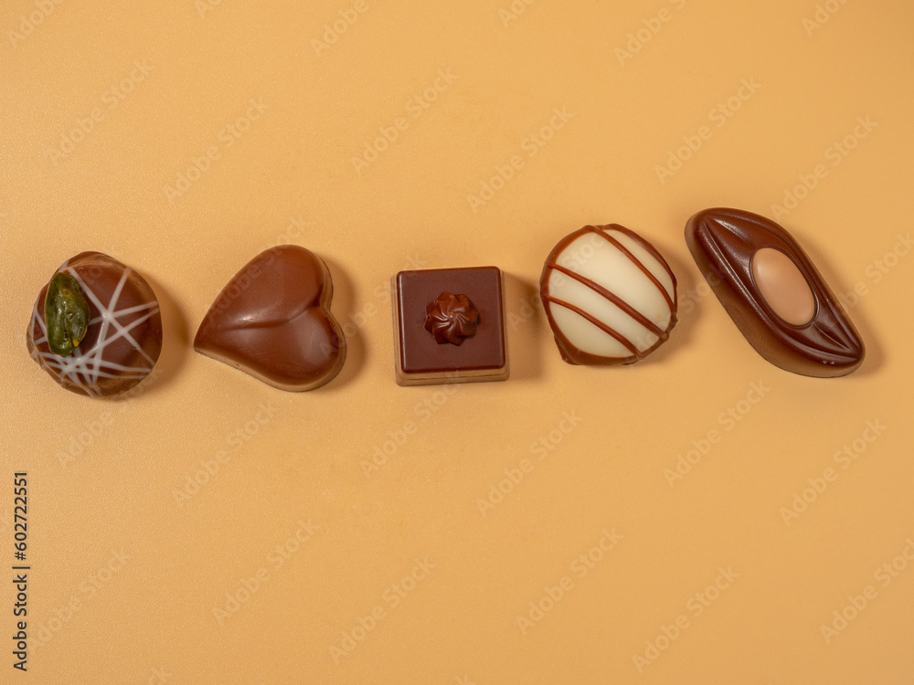 Assorted gourmet pralines in white, dark and milk chocolate. Chocolate candies on an orange background. Assorted gourmet pralines in white, dark and milk chocolate. Chocolate candies on an orange background.