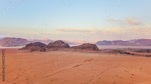 Orange red sand desert, rocky formations and mountains background, blue sky above, camp tents visible at distance - typical scenery in Wadi Rum, Jordan