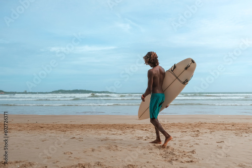 company of young guys Sri Lankans  Indians surfers on the ocean coast with a surfboard  sporty tanned body  smiling and running with a surfboard on the beach on a sunny summer day  ready to surf.