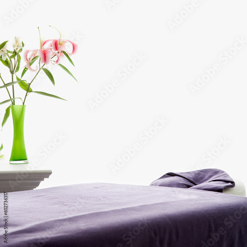 Tableau sur toile Spa scene of massage table with purple sheets and table with pink Easter lillies in green vase
