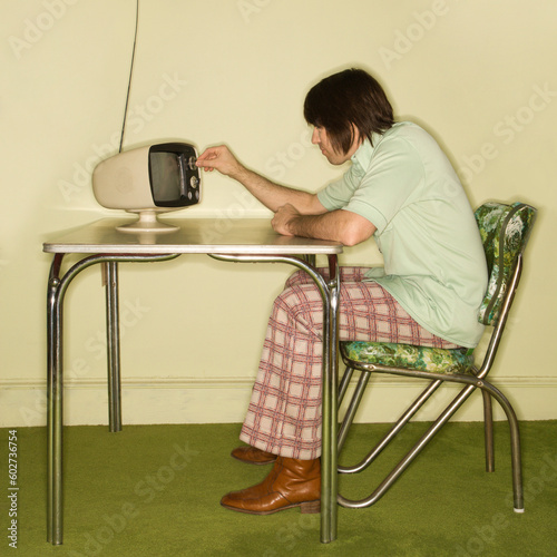 Side view of Caucasian mid-adult man sitting at 50's retro dinette set turning old television knob. photo