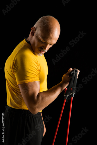 Mid adult multiethnic man wearing yellow exercise shirt exercising with stretch band and looking at bicep.