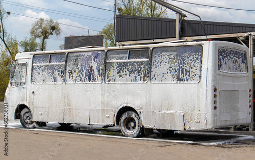 Big white bus in foam at a self-service car wash. External washing of public transport buses. Self-service manual high-pressure car wash in the open air.