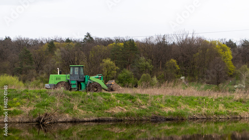 The tractor rides along the bank of a river or lake in the forest.