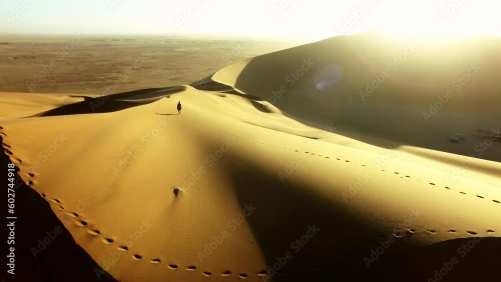 Travel, desert and silhouette of man at sunset with drone for destination, freedom or summer trip. Footprints, adventure and journey with guy on horizon of sand dunes on trip of Dubai vacation