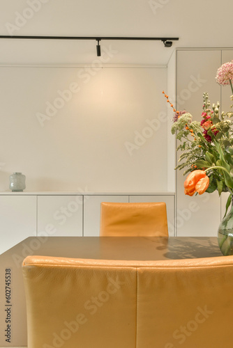 flowers in a vase on top of a table with two orange chairs and a white wall next to the room