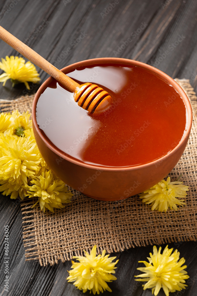 Honey with a dipper in a clay bowl and flowers on a dark wooden background. Honey with a dipper in a clay bowl and flowers on a dark wooden background.