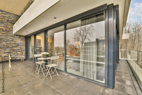 a patio with chairs and tables on the outside, looking out to the trees in the glass doors are open