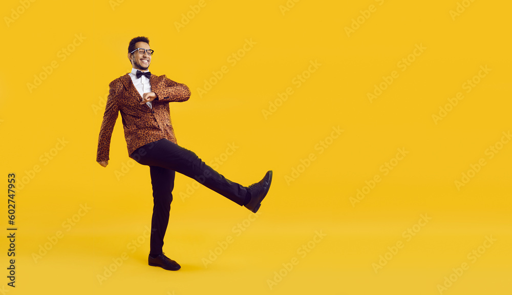 Full length studio shot of happy funny man. Cheerful young ethnic guy in extravagant leopard jacket with bowtie walking and smiling isolated on yellow colour advertising text copyspace background Full length studio shot of happy funny man. Cheerful young ethnic guy in extravagant leopard jacket with bowtie walking and smiling isolated on yellow colour advertising text copyspace background