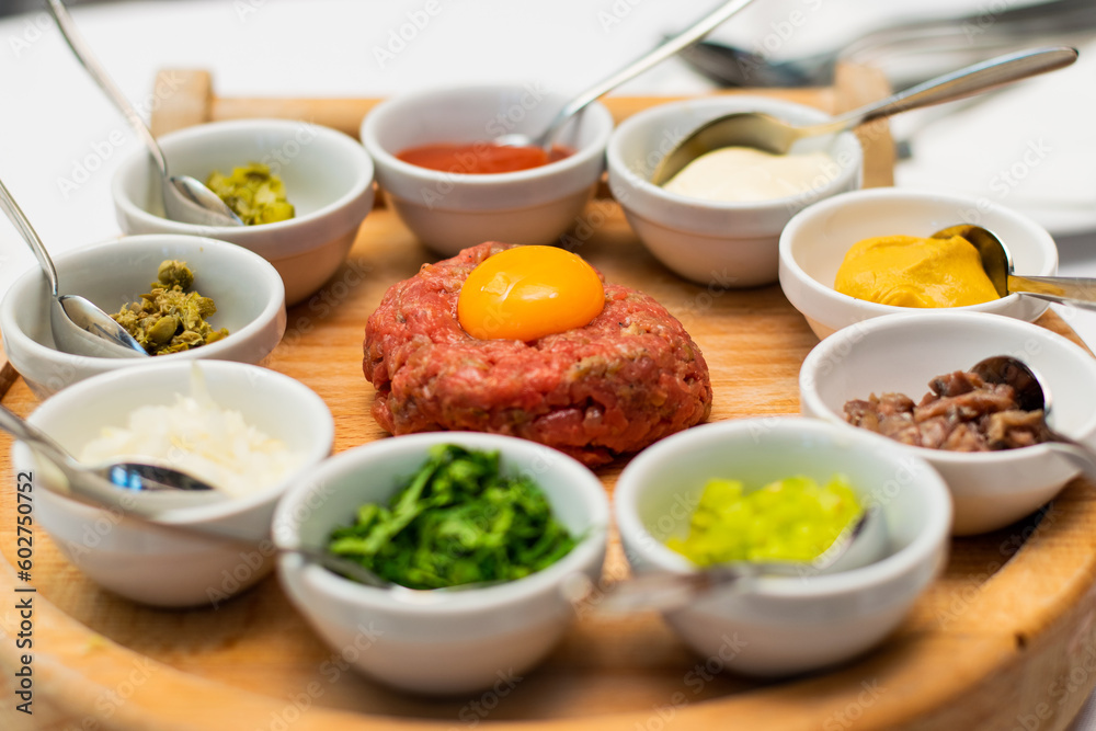 Restaurant waiter serving elaborate  - Beef tartare served on wooden board with various garnishes and egg yolk and person eats it