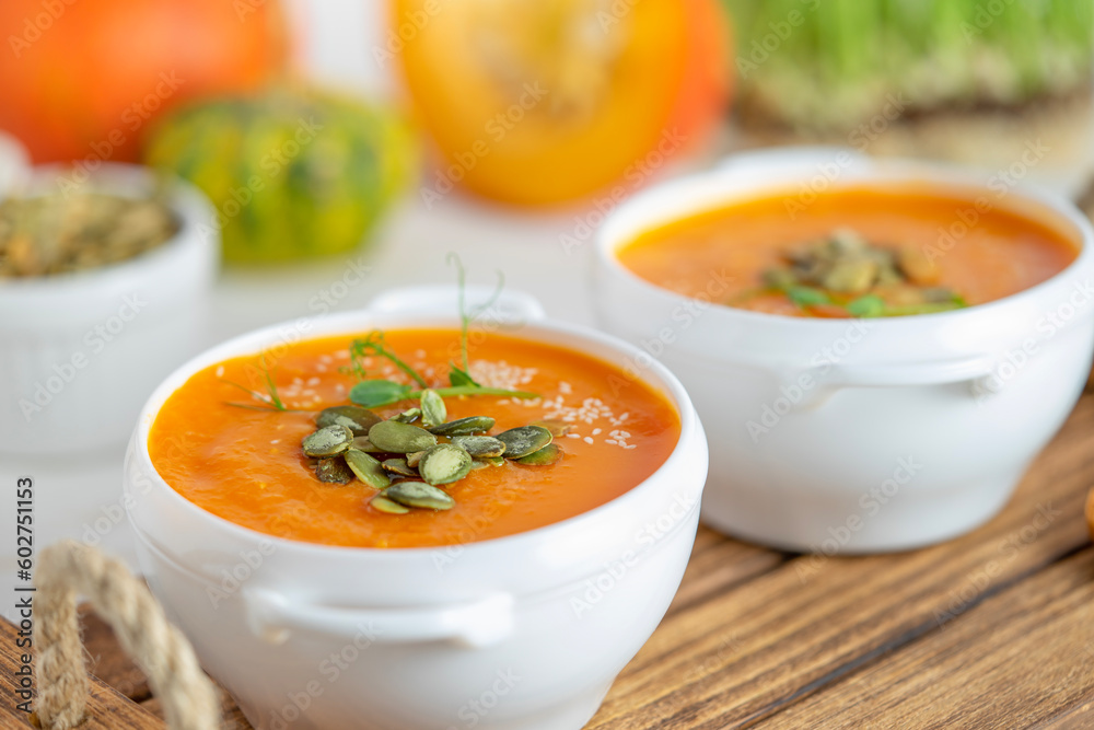 Pumpkin soup bowl with seeds on white wooden background. Close up