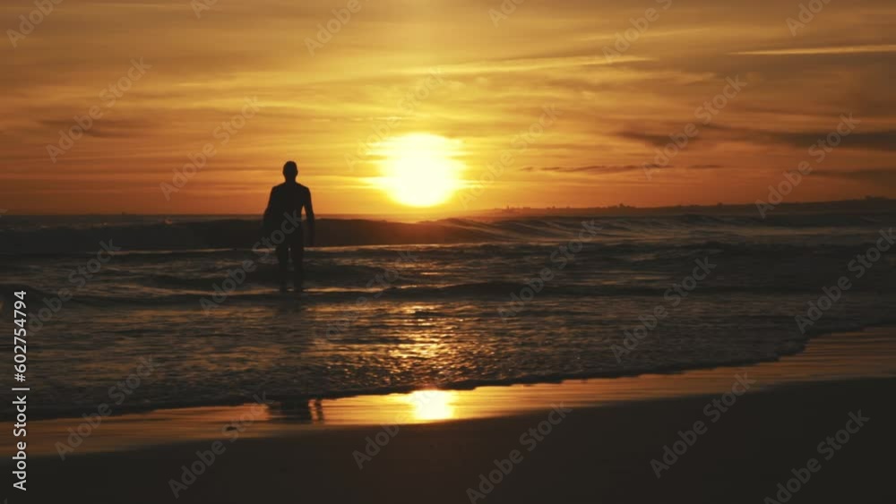 Silhouette of an athletic man standing on the seashore at sunset holding a surfing board Silhouette of an athletic man standing on the seashore at sunset holding a surfing board