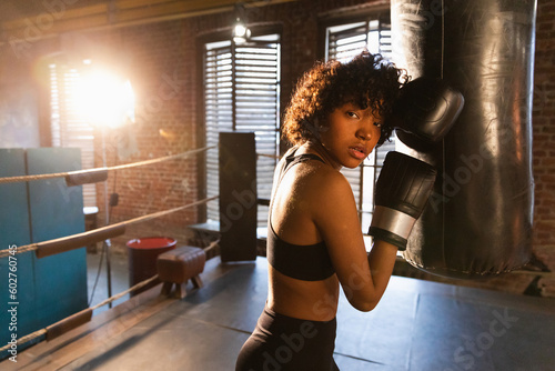 Fototapeta Naklejka Na Ścianę i Meble -  Women self defense girl power. African american woman fighter resting after fight training on boxing ring. Girl tired after punching boxing bag. Training day in gym. Strength fit body workout training