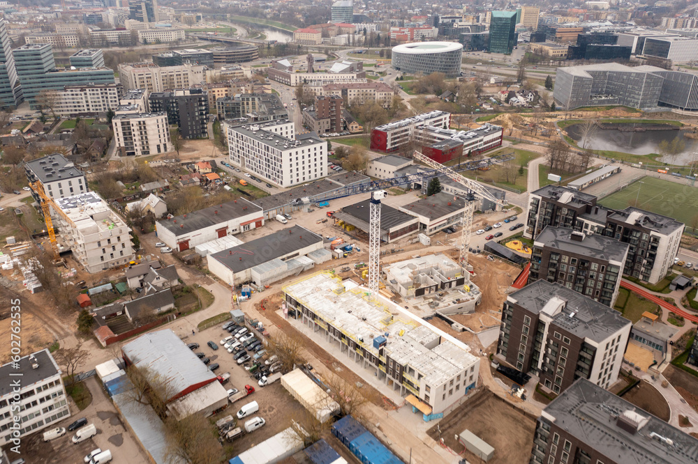 Drone photography of urban construction site of multistory apartment complex in the middle of other structures during spring sunny day. High angle view