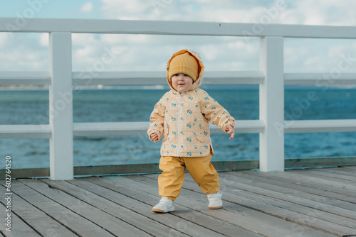 Obraz na płótnie A toddler in a yellow jacket and pants walks on the pier w salonie
