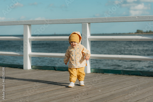 Obraz na płótnie A toddler in a yellow jacket and pants walks on the pier w salonie