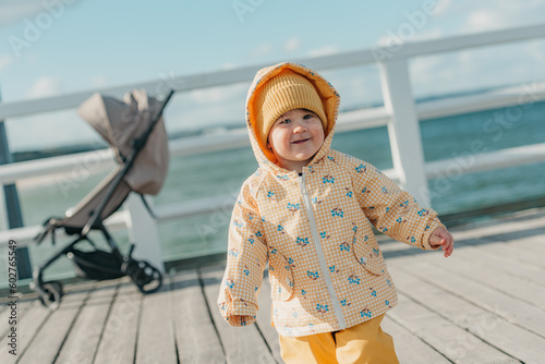 Obraz na płótnie A toddler in a yellow jacket and pants walks on the pier w salonie