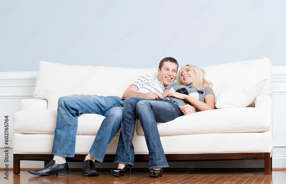 Full length view of affectionate couple laughing and relaxing together on white couch. Horizontal format.