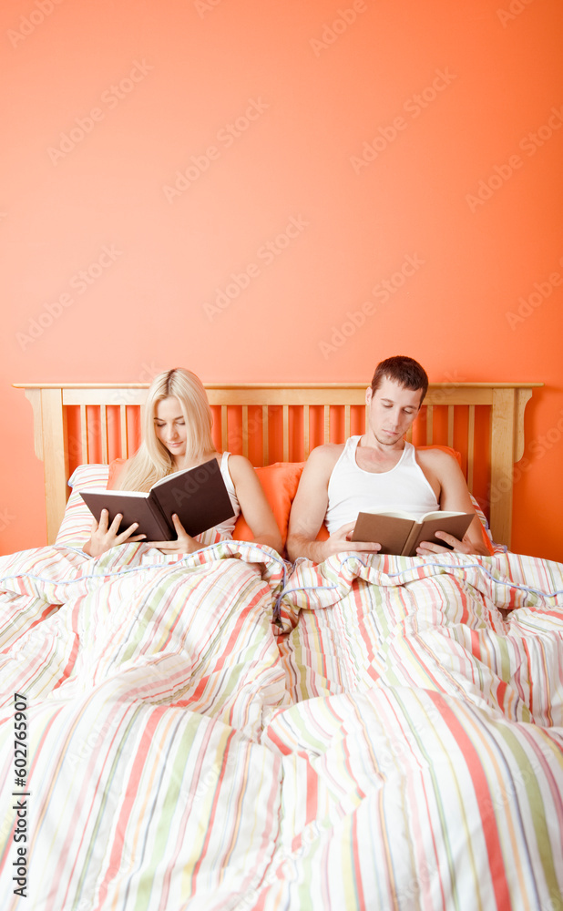 Man and woman reading side-by-side in bed. Vertical format.