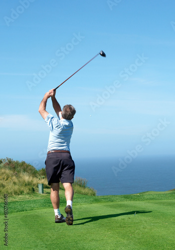 Senior male golfer playing golf from the tee box on a beautiful summer day next to the ocean
