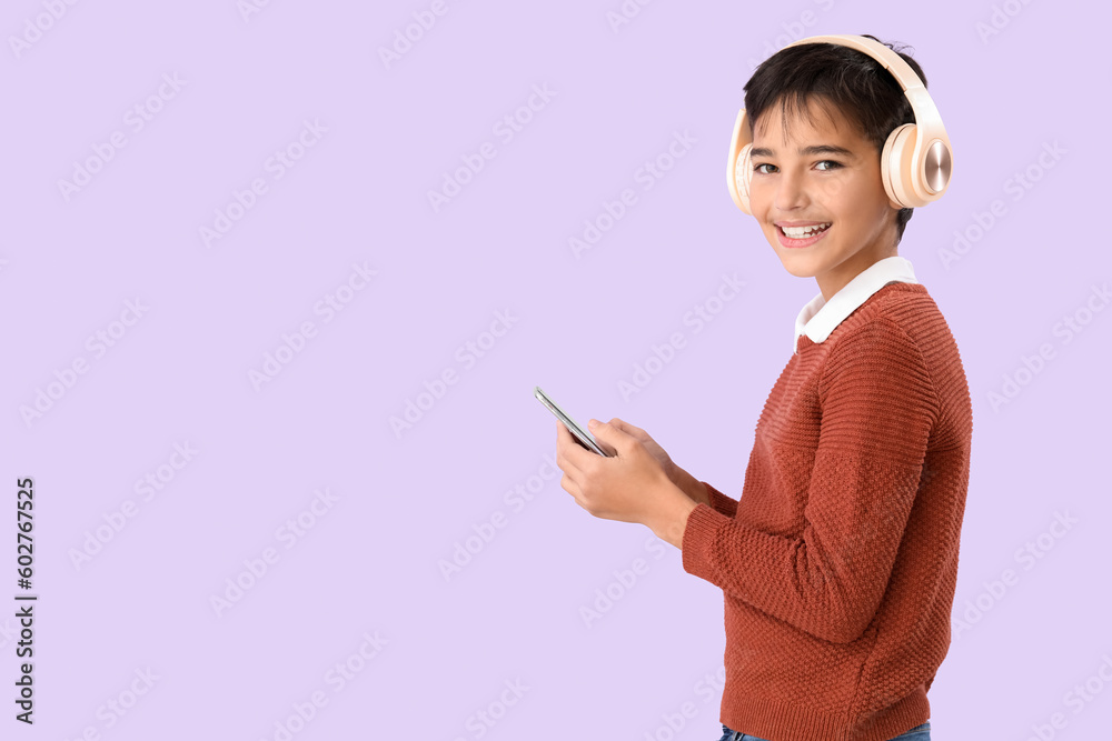 Little boy in headphones using mobile phone on lilac background Little boy in headphones using mobile phone on lilac background