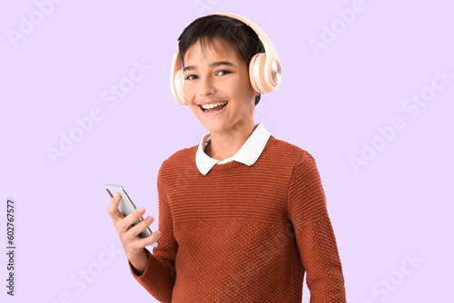 Little boy in headphones with mobile phone on lilac background